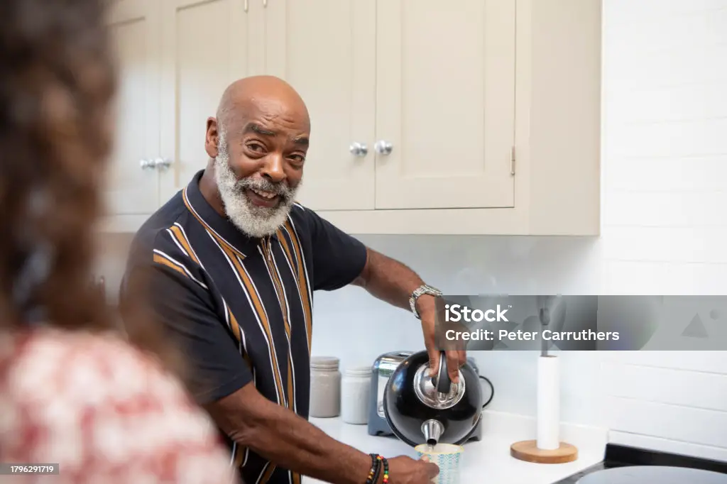 A man smiles at someone whilst pouring water from a kettle